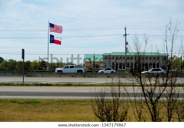 College Station,\
Texas / USA - March 23 2019: American and Texas flags across a\
highway with cars on the\
road.