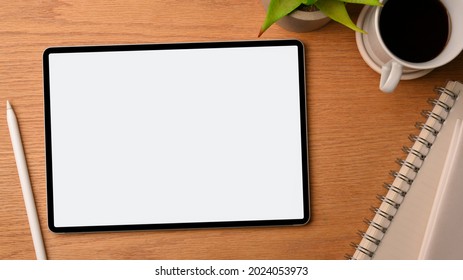 College Student Modern And Cozy Workspace Decorated With Wood Background, Digital Tablet Screen Mockup, Stylus Pen, Notepads, Black Coffee, Plant. Overhead View, Close Up