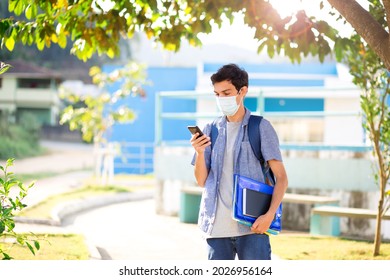 College Student Returning To College Or School And Wearing A Mask To Protect Himself From Covid-19. Using Cell Phone While Walking On College Campus.