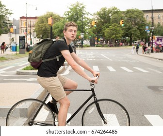 College Student Riding Bike Crossing The Crosswalk In The City, Photographed In Brooklyn, NY In July 2017