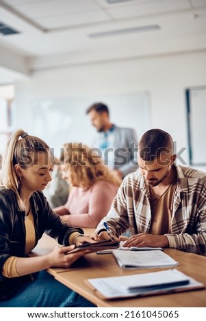 College student taking notes while studying with his female friend who is using touchpad in the classroom. 