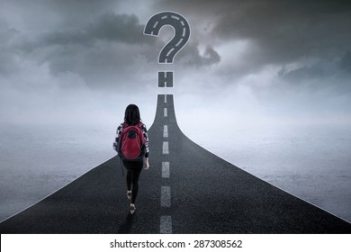 College student walking on the highway while looking at a question mark