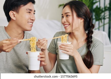 College Students Eating Instant Noodle From Plastic Cups With Chopsticks And Looking At Each Other