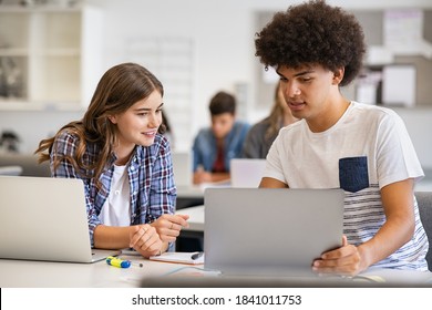 College students sitting together and using laptop during computer lesson. Black man and girl working on laptop in high school. Happy smiling multiethnic friends working on laptop for an assignment.