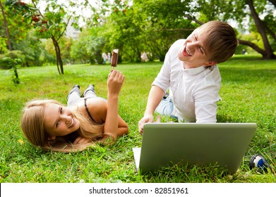 College Students Using Laptop On Campus Lawn And Eating Ice Cream