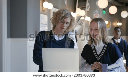 College students using laptop standing in campus corridor. High school boy and girl discuss science project on computer before lesson in hallway