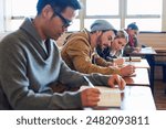 College students, writing and desk in classroom with books for english literature or language for exam. People, university and scholarship for learning or education, knowledge and academic work