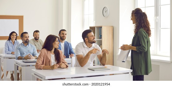 College teacher or business course trainer having discussion with group of people. Happy adult students sitting at tables in classroom, having training class and learning new things. Education concept - Shutterstock ID 2020121954