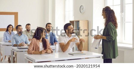 College teacher or business course trainer having discussion with group of people. Happy adult students sitting at tables in classroom, having training class and learning new things. Education concept