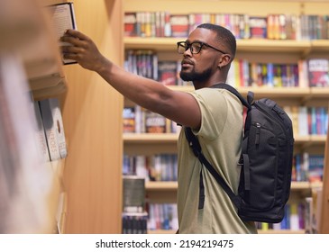 College Or University Student In A Library Taking A Book From The Shelf To Read And Study For Education. Reading, Learning And Academic Black Man Nerd At A Bookstore To Buy A Textbook