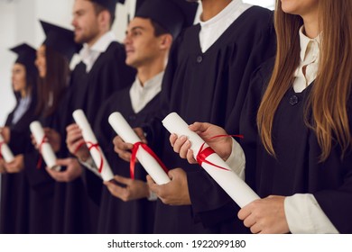 College or university students in black gowns holding traditional diploma scrolls at graduation ceremony. Happy graduates with certificates in hands celebrating milestone life event of getting degree