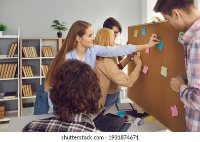 College Or University Students Working On Group Project. Creative Schoolmates Brainstorming In School Library, Exchanging Ideas, Writing Them On Colorful Sticky Notes And Pinning To Bulletin Board