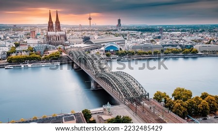 Cologne Aerial view with trains move on a bridge over the Rhine River on which cargo barges and passenger ships ply. Majestic Cologne Cathedral in the background