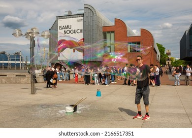 Cologne, Germany - May 17, 2022 : A Street Performer Making Gigantic Soap Bubbles In Front Of A Young Crowd Of People