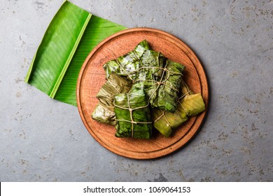 COLOMBIAN, CENTRAL AMERICAN FOOD. Tamales wrapped in banana palm tree leaves on wooden plates, gray stone background.