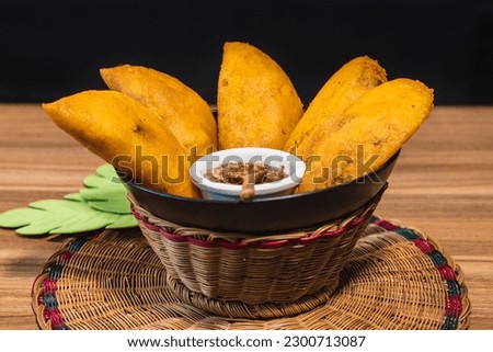 Colombian empanadas. Table with traditional Colombian food, wicker basket with empanada con aji, on a wooden table. black background.