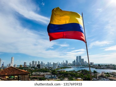 The Colombian flag waving in the wind. Blue sky with white clouds in the background. The city of Cartagena is in the far back. Shot in Cartagena, Colombia, USA. - Shutterstock ID 1317695933