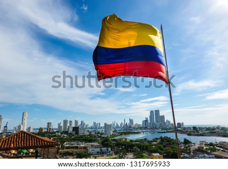 The Colombian flag waving in the wind. Blue sky with white clouds in the background. The city of Cartagena is in the far back. Shot in Cartagena, Colombia, USA.