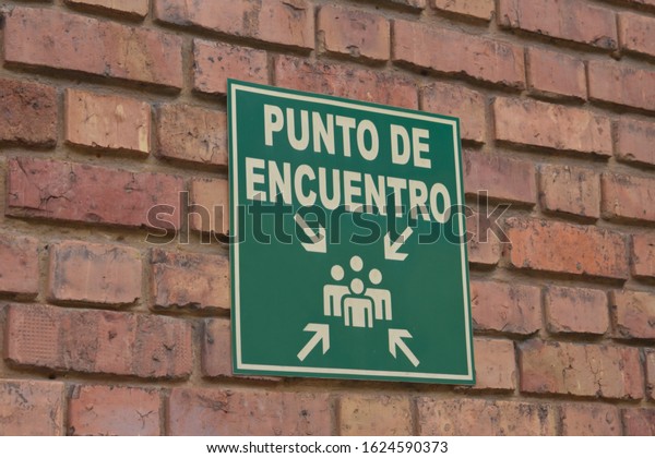 Colombian green\
emergency sing written in Spanish over an brick wall in Bogota.\
Translation: “meeting\
point.”