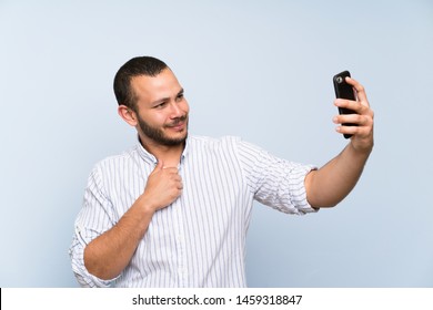 Colombian man over isolated blue wall making a selfie