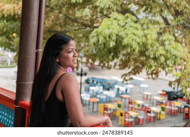 Colombian Woman Admiring Scenic Outdoor Cafe from Balcony - Powered by Shutterstock