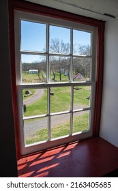 Colonial American Rural Village Lane And Buildings Seen Through An Antique Red 12-pane Pennsylvania Window With Sunlight Streaming In. Copy Space, No People.