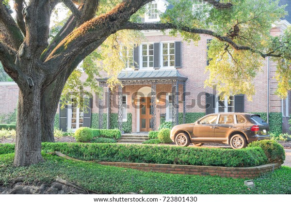 Colonial brick house with huge live oak\
tree and beautifully landscaped front yard. Car park under shady\
tree branches with warm backlit morning\
light.