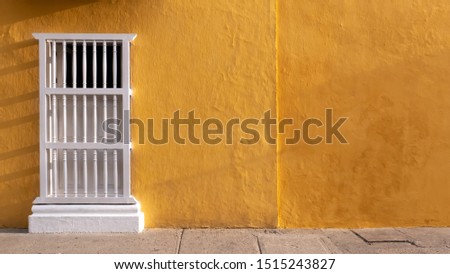 Colonial facade with ocher or yellow wall and window with white balusters, ideal for background, Cartagena de Indias, Colombia