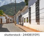 Colonial style houses line a cobblestone street in Santa Fe de Antioquia, Colombia, with lush green mountains in the backdrop