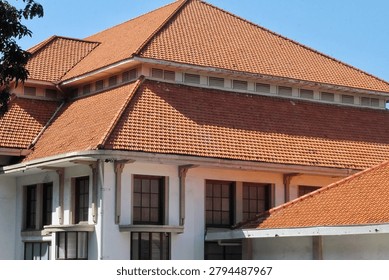 A colonial-style building featuring multiple red clay tiled roofs, large paneled windows and white stucco walls photographed against a clear blue sky