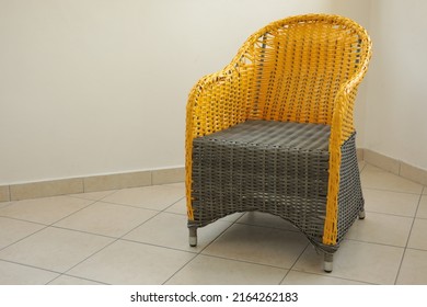 Color Blocking Wicker Armchair Made From Grey And Yellow Color Plastic Faux Rattan. Empty Woven Chair On Tiled Floor. Patio Furniture On Beige Wall Background. Interior Mockup With Copy Space