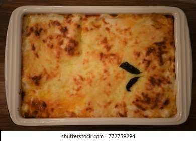 Color Food Photography Image Of Cooked Homemade Lasagna For Family Dinner Ready For Eating Served In A Cream Dish And On Wood Background With Melted Cheese Top And Basil Leaves