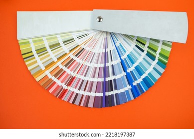Color guide close up. Assortment of flowers for design. Color palette fan on orange background A graphic designer chooses colors from a color palette guide. Color swatch catalog