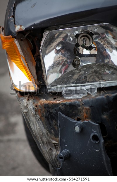 Color image\
of a crashed car with broken\
headlight.