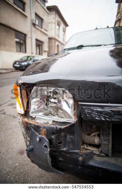Color image\
of a crashed car with broken\
headlight.