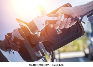 Color image of a man's hand preparing to charge an electric car.