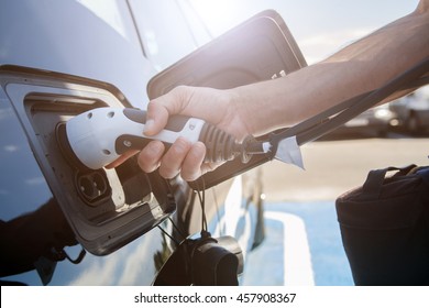 Color image of a man's hand preparing to charge an electric car.
