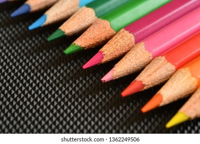 Color pencils on black rubber background. Close-up.