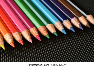 Color pencils on black rubber background. Close-up.