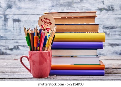 Color Pencils In A Red Cup. Pile Of Coloured Books. Congratulation For Best Teacher.