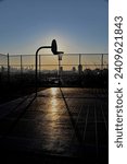 color photo of outside basketball court and hoop silhouetted during sunrise in an urban setting