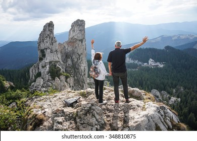 Color picture of an elderly couple holding hands and waving on top of a mountain - Powered by Shutterstock