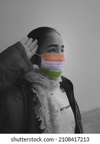 Color pop image of an indian girl saluting and looking upward with a tricolor mask on her face. Useful image for national days or republic day or army related content. 