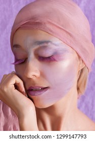 Color portrait of beautiful woman wearing fantasy artistic makeup and purple lashes with a pink head scarf, posing in front of a purple background. - Shutterstock ID 1299147793