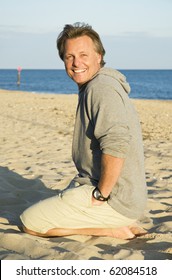 A Color Portrait Photo Of A Happy Smiling Man In His Forties Kneeling Down On The Beach.