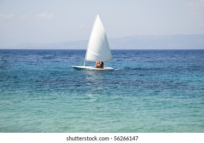 A color portrait photo of a white sailing dinghy sailing across a beautiful turquoise sea.
