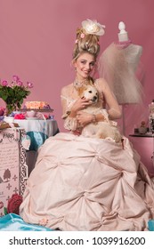 Color portrait of woman dressed as Marie Antoinette in pink with a cute puppy on her lap