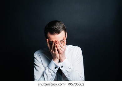 Color Portrait Of A Young Man In A Shirt And Black Tie, Upset, Hands On His Face, Against Plain Studio Background