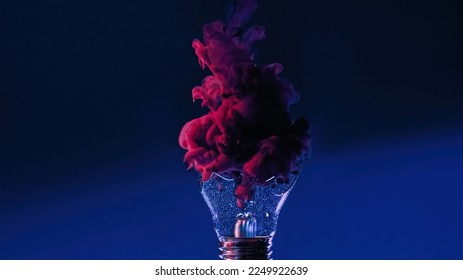 Color smoke in broken lamp. Ink water. Pink paint fluid shot vapor cloud in crashed glass light bulb on dark navy blue abstract copy space background.