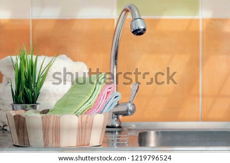Color towels in wooden bucket on stainless  sink with tap water in the kitchen